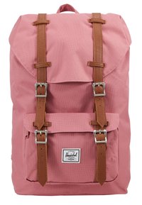 Sac à dos en toile rose avec des sangles et boucles en cuir marron. Il dispose d'une fermeture à rabat et d'une poche avant. Logo Herschel sur le devant.