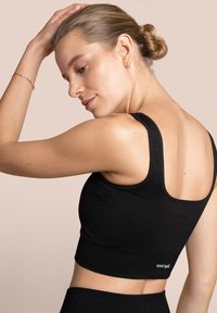 Czarny prążkowany crop top z szerokimi ramiączkami, o dopasowanym fasonie i bezszwowym wykończeniu. Mały detal z logo na tylnym końcu.