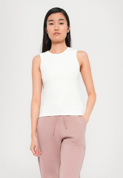 White sleeveless top with a round neckline, smooth texture, fitted design, paired with light pink jogger pants featuring side pockets.