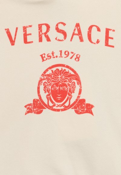 Κόκκινο λογότυπο Versace με κεφάλι Μέδουσας και κείμενο "Est. 1978" σε μπεζ υφασμάτινο φόντο.