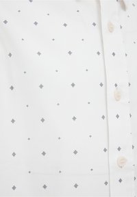 Vit skjorta med uppknäppt krage som har ett geometriskt mönster av marinblå prickar och linjer. Mjuk tyg, klassisk krage och pärlliknande knappar.