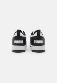 Pár černobílých tenisek Puma z pohledu zezadu, s tlustými bílými podrážkami a značkovými patkami na jednobarevném pozadí.