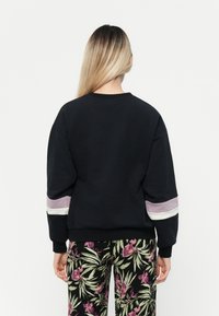 Sudadera negra con rayas de colores en las mangas, escote redondo, puños acanalados y corte relajado, combinada con pantalones de patrón floral.