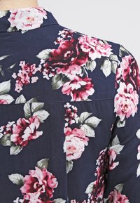 Floral shirt featuring a dark navy background with large pink and white roses, accented by green leaves, smooth fabric texture, and collar detail.