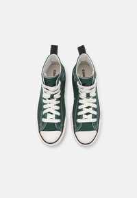 Ψηλές αθλητικές μπότες από πράσινο καμβά με λευκές κορδόνες, λευκό καπάκι από καουτσούκ στη μύτη και μαύρες λεπτομέρειες. Διαθέτει κεντημένο λογότυπο στο πλάι.