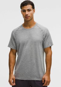 Tricou sport cu mâneci scurte, de culoare gri, cu un model texturat, decolteu rotunjit și mâneci raglan. Materialul pare ușor și respirabil.
