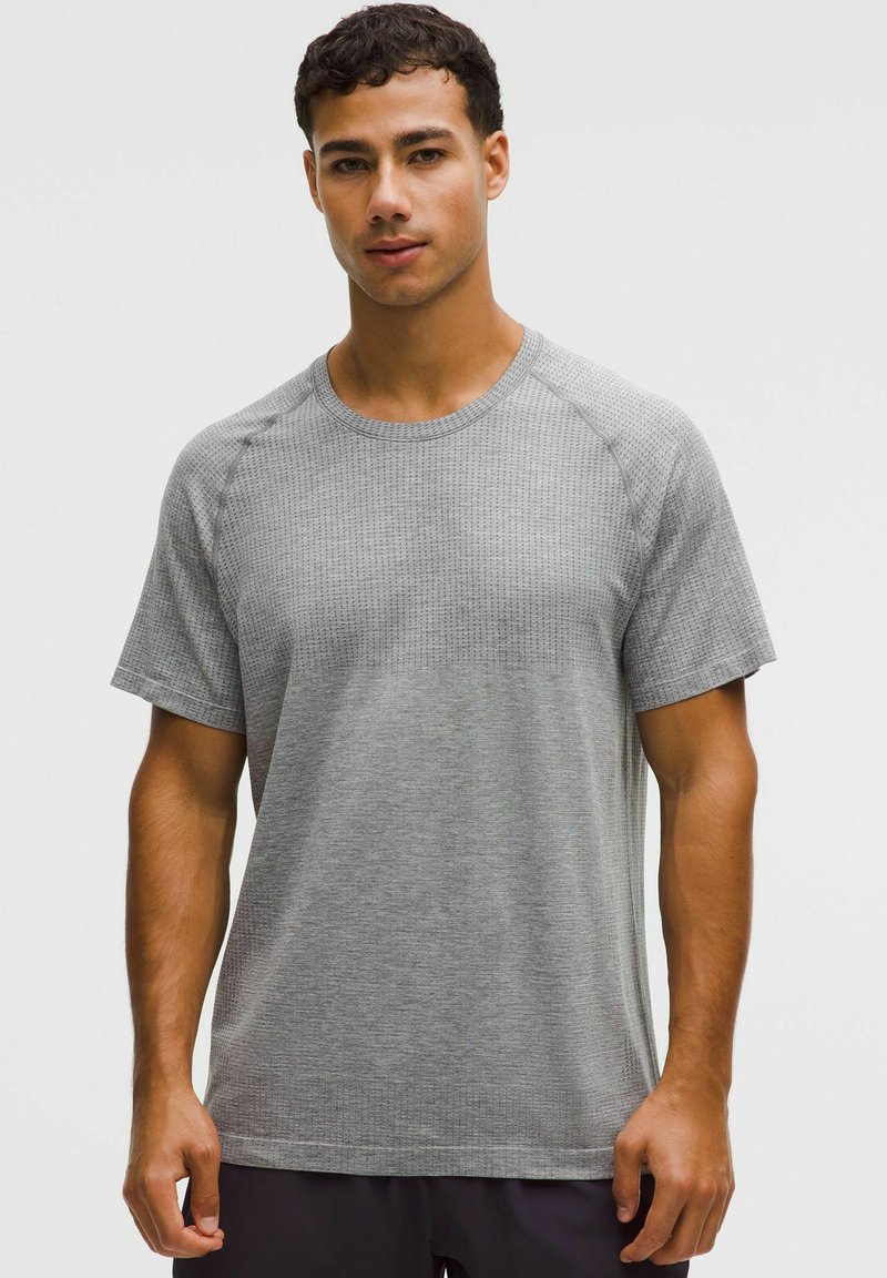 Tricou sport cu mâneci scurte, de culoare gri, cu un model texturat, decolteu rotunjit și mâneci raglan. Materialul pare ușor și respirabil.