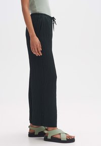 Zwarte geribbelde palazzo-broek met een elastische tailleband en trekkoord, gecombineerd met groene sandalen met een brede band en een platte zool.