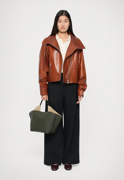 Brun læder cropped jakke med bred krave, parret med sorte bukser med vidde. Holder en grøn og beige struktureret tote taske.