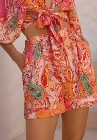 Ensemble deux pièces avec un motif cachemire orange, rose et vert. Le haut a un devant noué et des manches courtes ; le short comporte des poches.