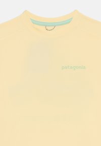 Žaliai geltonos spalvos Patagonia trumpas rankovėm marškinėliai su apvalia iškirpte, apibriestais švelnia mėlyna vidine apdaila ir mažu žaliu logotipu priekyje.