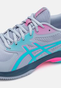 Chaussure de sport gris clair avec des accents turquoise et rose. Tige en mesh, panneaux texturés et semelle flexible. Comprend des lacets et une marque bien visible.