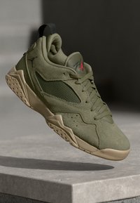 Zapatilla deportiva en verde oliva con material de ante y malla, diseño de cordones, collar acolchado y suela de goma con acentos en forma de puntos.
