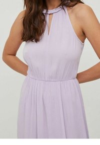 Femme portant une robe lavande sans manches avec un col en forme de goutte et une taille froncée, debout les mains derrière le dos.