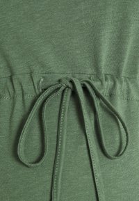 Green cotton fabric with gathered waist featuring a drawstring. The texture is smooth, with a consistent knit pattern visible throughout.