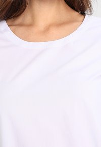 T-shirt blanc en coton avec un col rond et une texture lisse, doté de manches courtes et sans motifs ni ornements visibles.