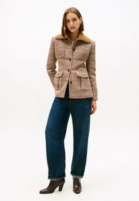 Geruite jasje met een bruine suède kraag, getailleerde pasvorm, voorzakken, zwarte knopen, gecombineerd met wijde donkerblauwe jeans en bruine haklaarzen.
