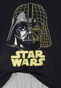 Black t-shirt featuring a graphic of Darth Vader's helmet in gray and yellow with the text "STAR WARS" in bold yellow beneath.