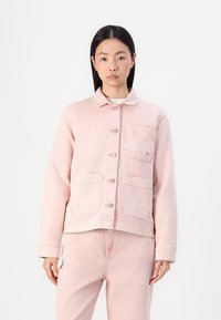 Chaqueta de mezclilla rosa con cuello, que cuenta con bolsillos frontales y botones. La tela tiene una textura suave y un acabado ligeramente desgastado.