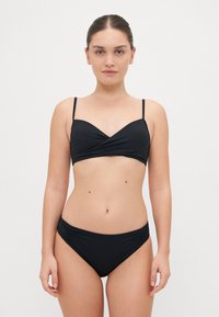 Black bikini set featuring a wrap-style top with thin straps and gathered sides on the bottom. Smooth, stretchy fabric with a matte finish.