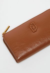 Portafoglio marrone con texture in pelle, dotato di chiusura con zip e una cerniera di metallo color oro, con logo impresso sul davanti.