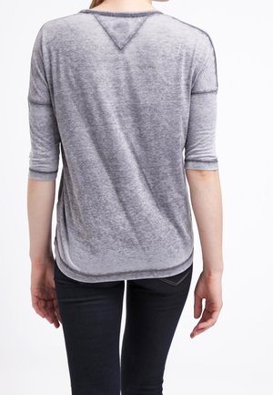 Camisa gris de manga corta con una textura suave y ligeramente transparente, y un dobladillo redondeado, que presenta un sutil escote en forma de V y detalles de costura.