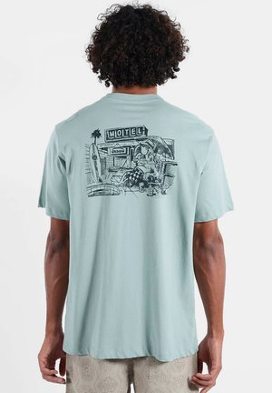 T-shirt à manches courtes couleur turquoise clair avec un imprimé graphique noir représentant une scène de motel au dos. Tissu doux, coupe décontractée, col rond.