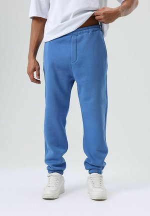 Lichtblauwe joggingbroek gemaakt van zacht stof, met een elastische tailleband, taps toelopende boorden en zijzakken. Gecombineerd met witte sneakers.