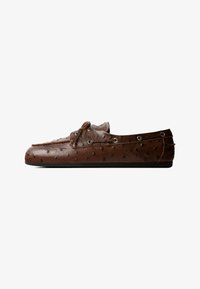 Mocasín de cuero marrón con patrón texturizado, detalle de cordones en la parte superior, ojales metálicos y suela plana negra.