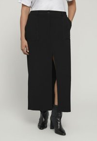 Fustă midi neagră cu o fendue frontală, dotată cu două buzunare frontale și o talie ajustată, asortată cu bote negre cu toc la gleznă.