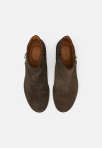 Paire de bottines en daim marron foncé avec fermetures éclair latérales et boucles, semelles intérieures en cuir beige, vues de dessus sur fond blanc.