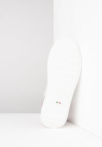 Semelle de sneaker blanche avec des rainures horizontales, présentant une légère courbure. Elle arbore un petit drapeau italien près du talon. Texturée pour une meilleure adhérence.
