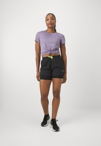 Tricou scurt, mov, cu un nod în față, și pantaloni scurți negri cu șnur. Pantofi sport negri cu accente verzi neon.