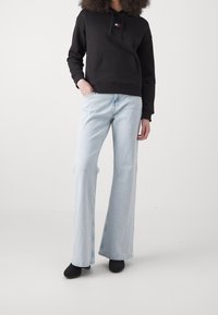 Černá mikina s kapucí a přední kapsou, doplněná o světle modré široké džíny. Černé boty dokončují celý outfit.