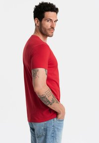 Rød kortærmet t-shirt i bomuldsstof, med et tætsiddende design og rund halsudskæring. Modellen har lys blå denim jeans på.