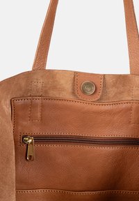 Innenraum einer tan-farbenen Leder-Tasche mit glatter Textur, einer Reißverschlusstasche mit goldfarbenem Reißverschluss und einem Druckknopfverschluss oben.