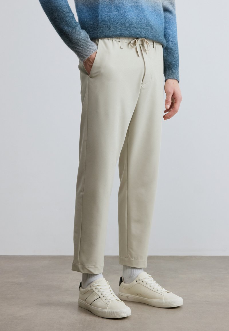 Beiget kapeat housut, joissa on joustava vyötärönauha ja kiristysnauha, sivutaskut ja resorit lahkeensuissa. Yhdistetty kermanvärisiin tennareihin ja valkoisiin sukkiin.