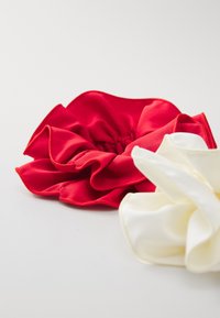Punaiset ja valkoiset kangaslenkit, joissa on rypytty liitos. Punaisella on sileä pinta, kun taas valkoisessa on hieman kiiltävä viimeistely.