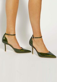 Green patent leather high-heeled shoes with a pointed toe and ankle strap. Features a cut-out side design and slender stiletto heel.