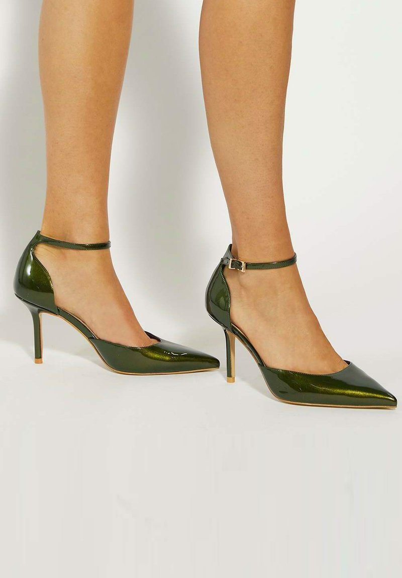 Green patent leather high-heeled shoes with a pointed toe and ankle strap. Features a cut-out side design and slender stiletto heel.