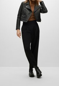 Sort læder bikerjakke med lynlåse, brun tætsiddende top og sorte skræddersyede bukser. Sorte ankelstøvler fuldender outfittet.