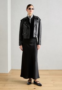 Black leather biker jacket over a long, fitted black dress. Features a patterned black and white scarf and black flat shoes. Minimalist design.