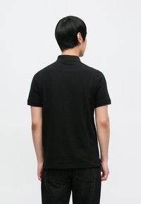 Črna polo majica s kratkimi rokavi, ravnim krojem, bombažno tkanino, rahlo teksturo, s standardnim ovratnikom in diskretnimi šivnimi detajli.