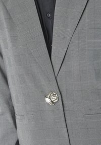 Gråternet blazer med en struktureret design, tekstureret stof og en fremtrædende sølvfarvet knap i form af en løve.