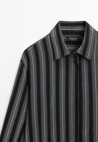 Chemise noire à boutons avec des rayures verticales blanches et grises et un col pointu, étiquetée Massimo Dutti, fabriquée au Portugal.