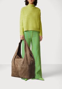 Brown suede hobo bag with soft texture, curved top, and single strap held by a person wearing a bright green sweater and striped pants.