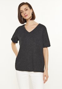 Sort kortærmet V-hals t-shirt med et tekstureret mønster. Løs pasform med opkrøllede ærmekanter. Sammen med lyse bukser.