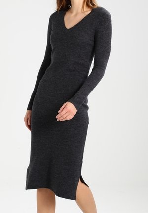 Frau trägt ein eng anliegendes, langärmeliges, dunkelgraues gestricktes Midikleid mit V-Ausschnitt und kleinem Seitenschlitz am Saum.