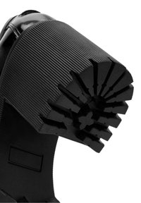 Semelle de chaussure noire avec un talon épais présentant des rainures et des crêtes radiales profondes pour une meilleure adhérence sur une surface lisse.