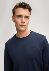 Marineblaues Langarm-Crewneck-Pullover aus weichem Material, mit einem strukturierten gestickten Logo auf der linken Brust und einem gerippten Kragen.